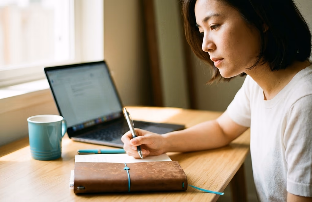 Person drafting a compelling LinkedIn About section in a notebook beside a laptop
